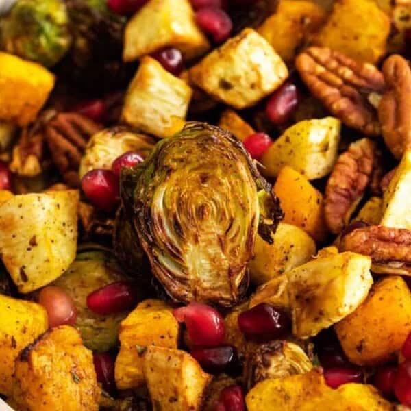 A bowl filled with roasted Brussels sprouts, squash, and parsnips, mixed with pecans and pomegranate seeds.