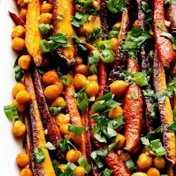 A white platter with roasted carrots, chickpeas, fresh parsley, and green onions.