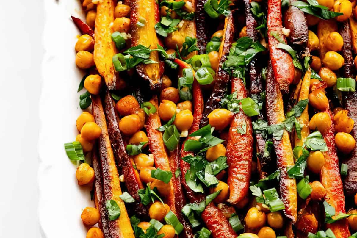 A white platter with roasted carrots, chickpeas, fresh parsley, and green onions.