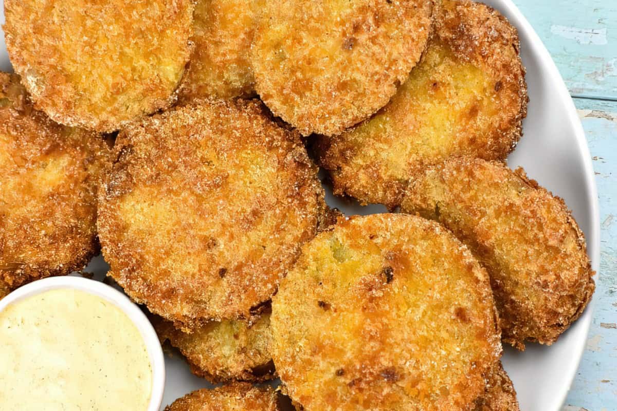 A plate of golden-brown fried green tomatoes accompanied by a small dish of creamy dipping sauce.