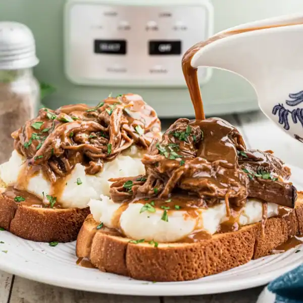 Two slices of bread with mashed potatoes and shredded beef topped with gravy on a white plate; salt and pepper shakers behind.