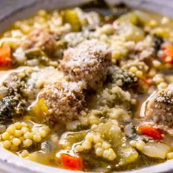 A bowl of Italian wedding soup with meatballs, small pasta, mixed vegetables, and grated cheese sprinkled on top.