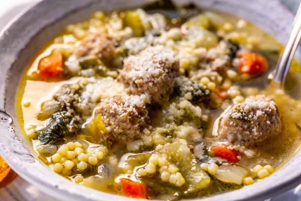 A bowl of Italian wedding soup with meatballs, small pasta, mixed vegetables, and grated cheese sprinkled on top.