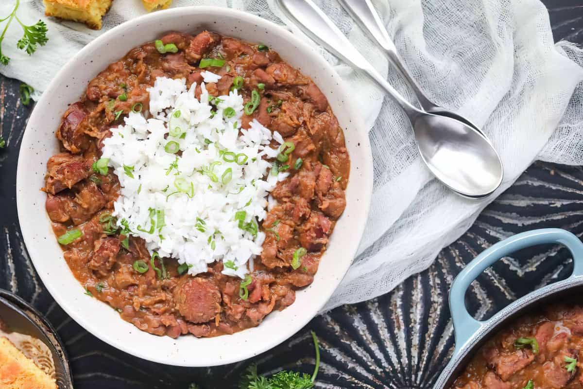 A bowl of red beans and rice garnished with chopped green onions, with spoons nearby.