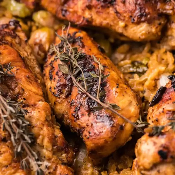 Close-up of roasted chicken breasts with fresh thyme on top, served over seasoned rice and assorted vegetables.