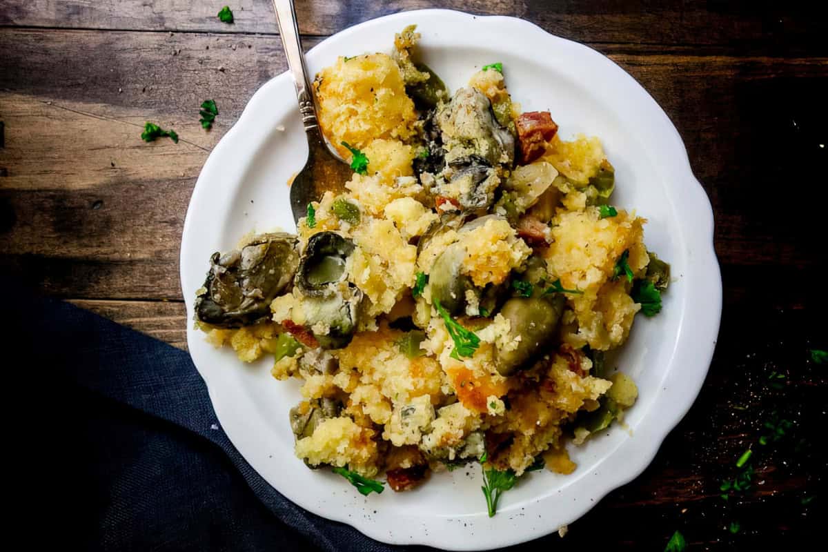 A plate of oyster dressing with a fork, featuring oysters, crumbled bread, and garnished herbs.
