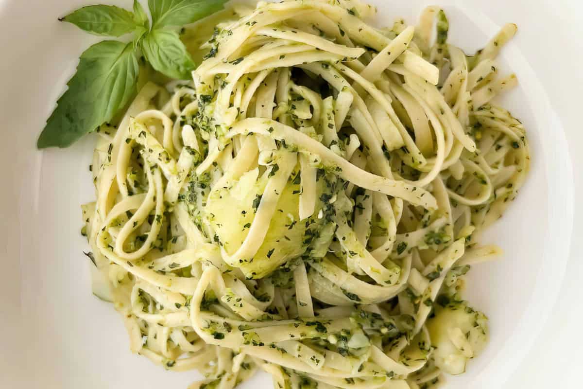 A plate of fettuccine pasta with pesto sauce and a sprig of fresh basil.