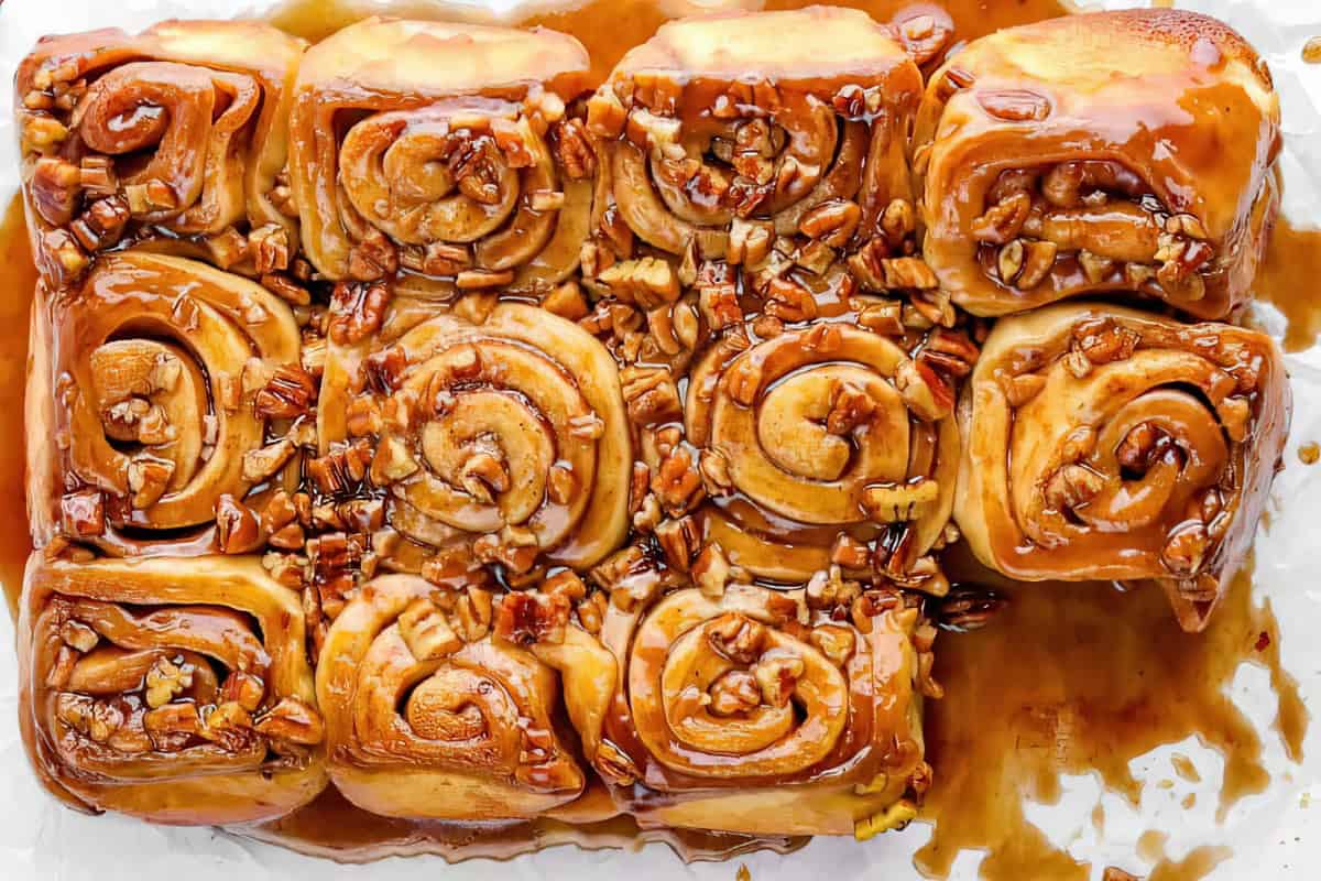 Nine glazed cinnamon rolls topped with chopped pecans arranged on a tray.