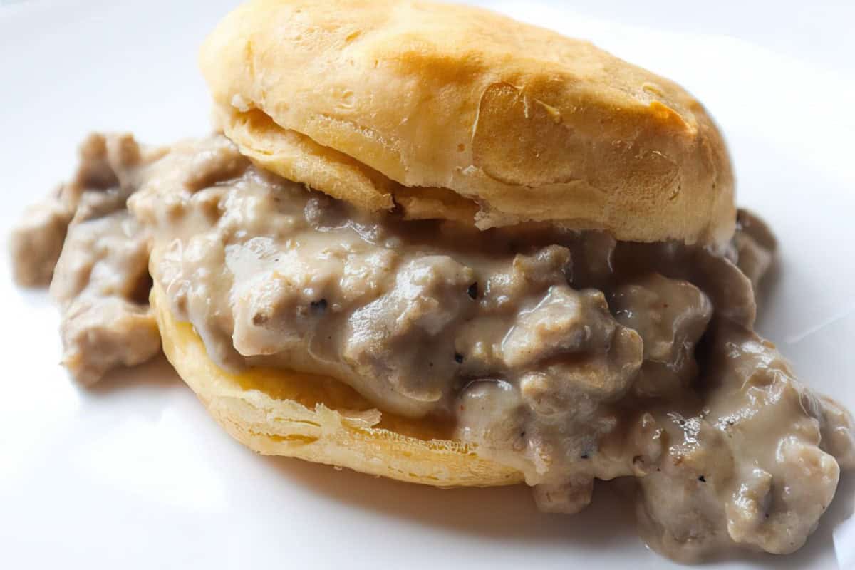 A white plate featuring a biscuit covered in creamy sausage gravy.