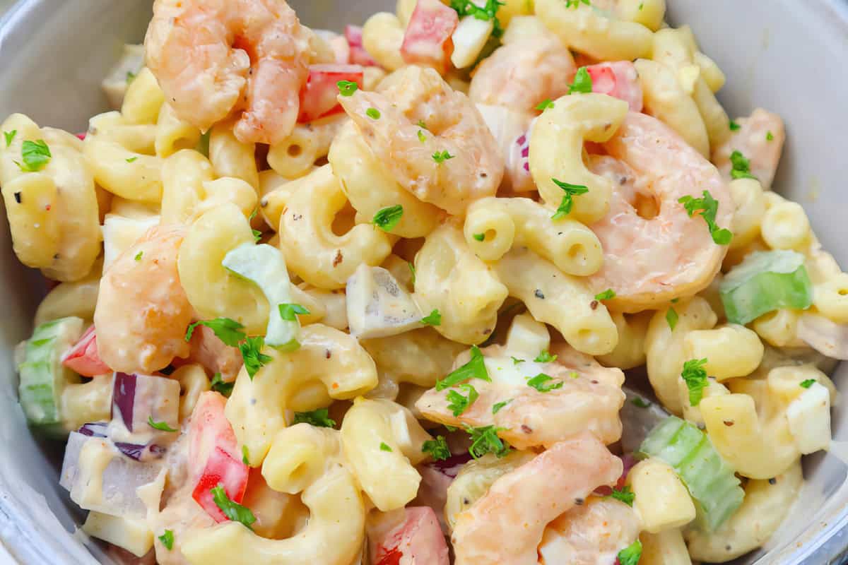 A bowl of macaroni salad with shrimp, chopped celery, red onion, and red bell pepper, garnished with parsley.