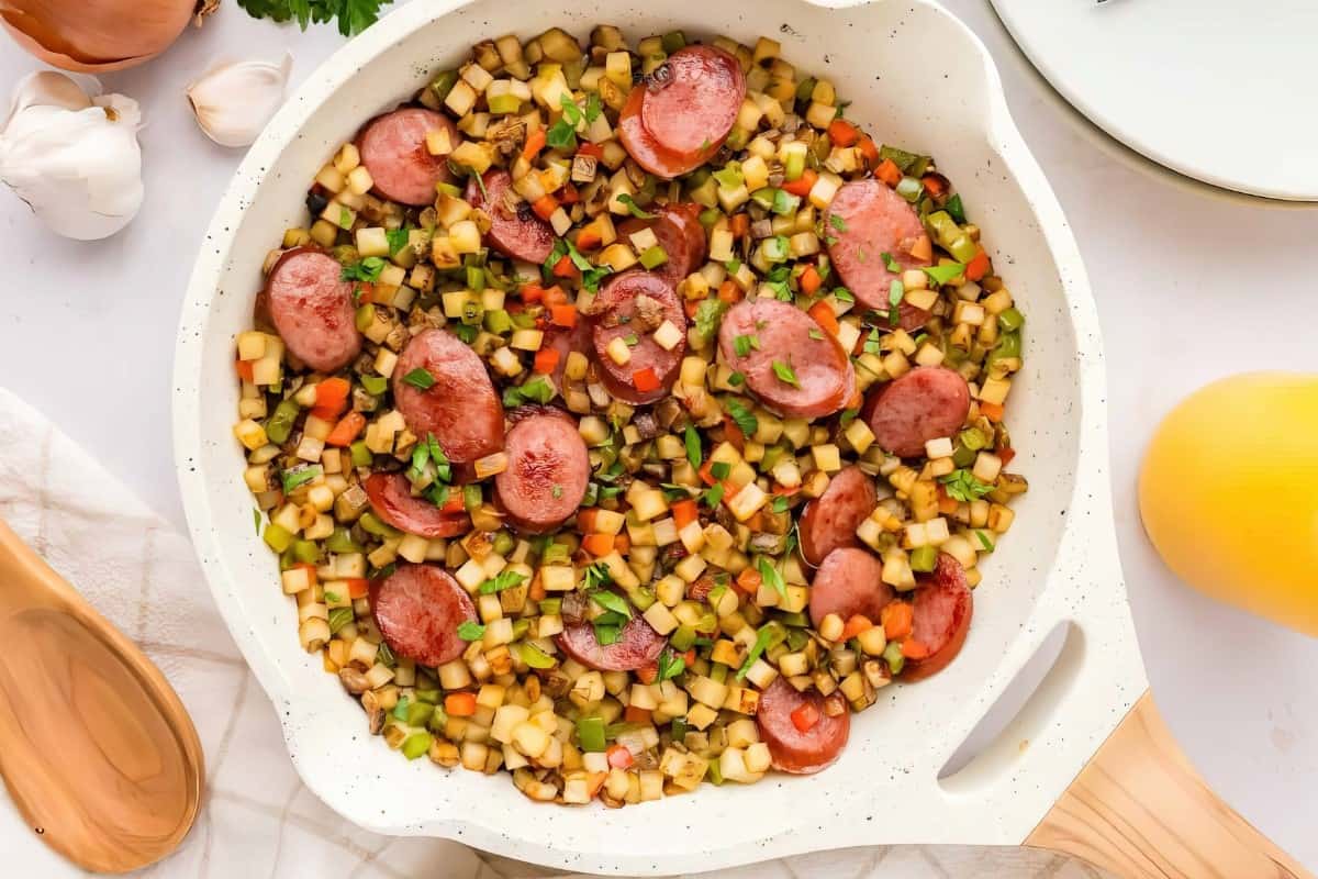 The image shows a skillet containing diced vegetables and sliced sausage.