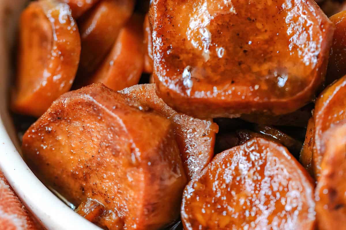 A close-up view of candied sweet potatoes in a dish, featuring a shiny, caramelized coating.