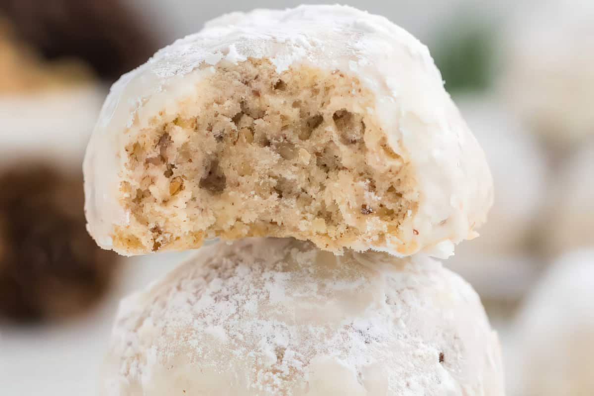 A stack of powdered sugar-coated cookies, with the top cookie showing a crumbly interior.