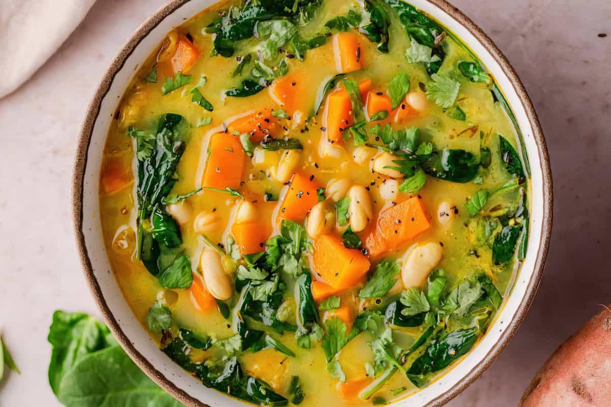 A bowl containing spinach, sweet potatoes, white beans, and herbs, garnished with black pepper and cilantro.