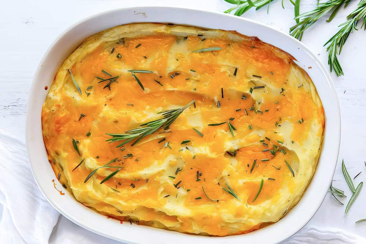 An oval white dish containing creamy mashed potatoes topped with rosemary sprigs.