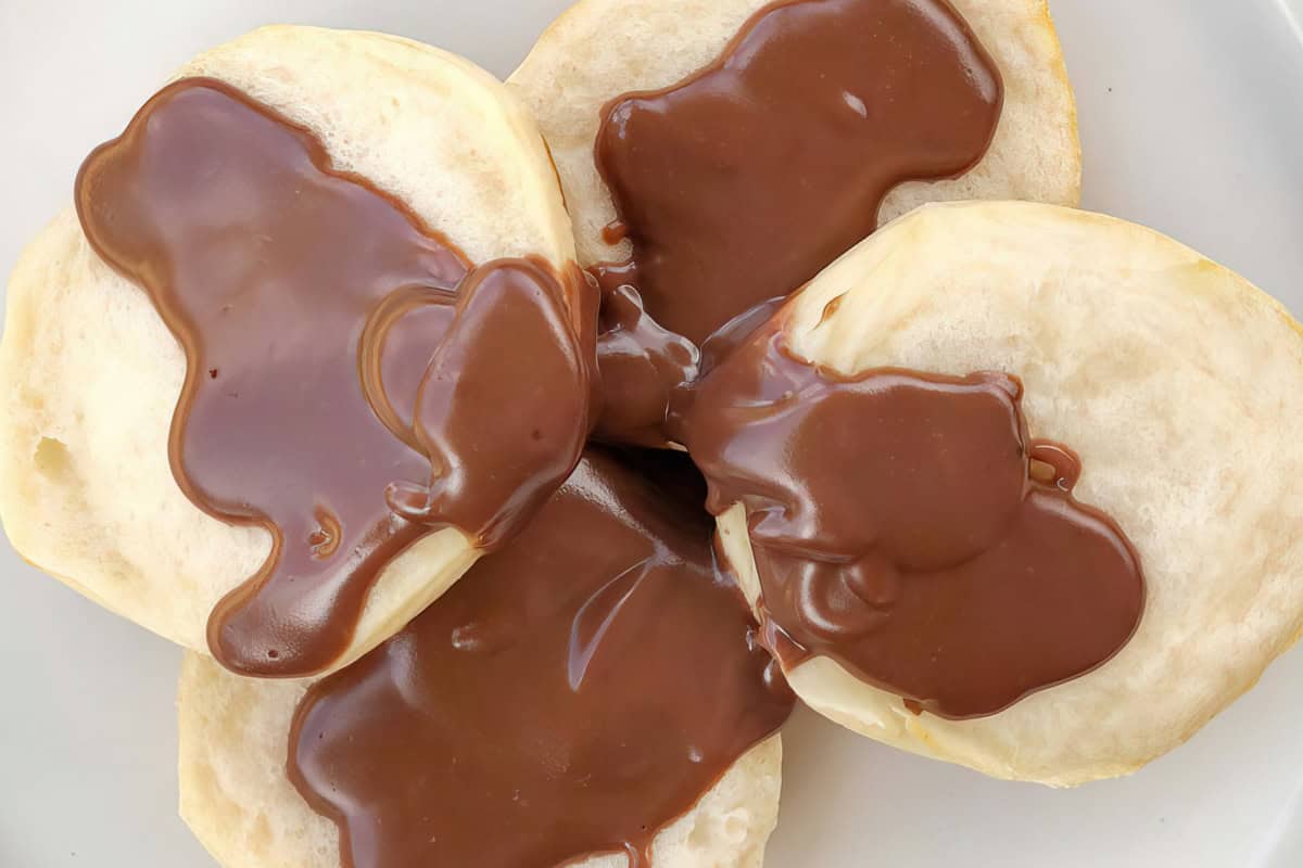Round pastries with glossy chocolate sauce on a white plate.