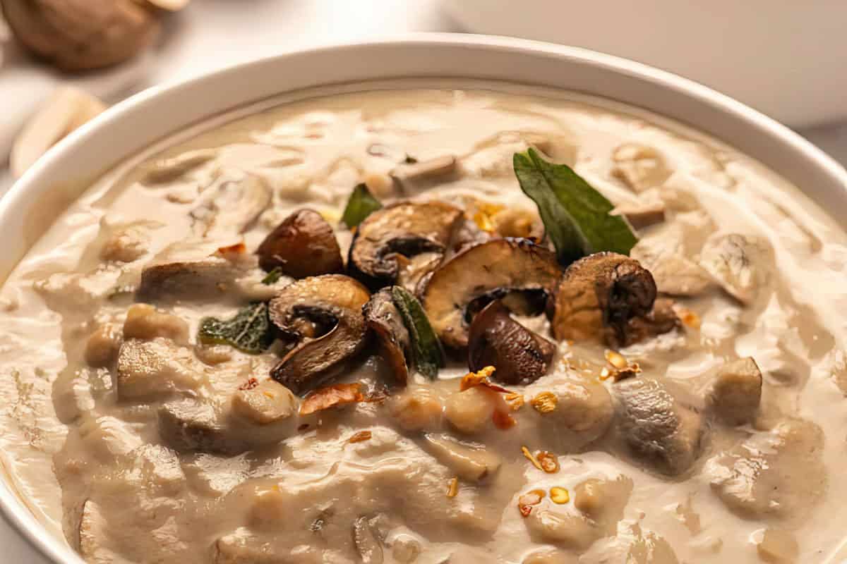 A bowl of soup with sliced mushrooms and herbs on top.