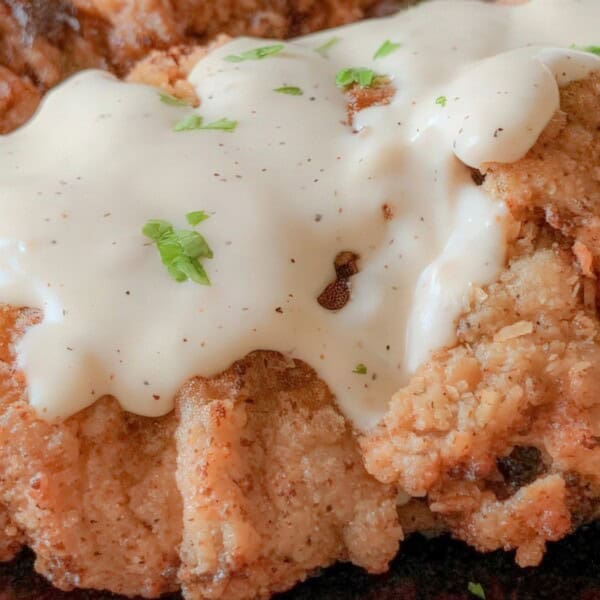 Crispy fried chicken topped with creamy white gravy and sprinkled with chopped green herbs.