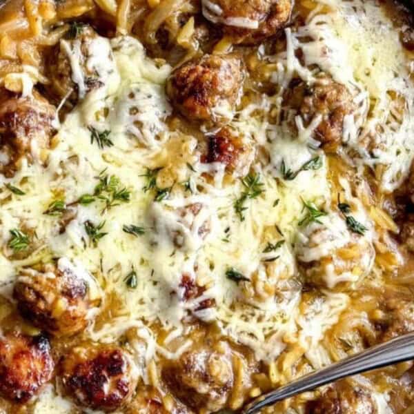 The image shows a pan containing melted cheese, meatballs, and herbs on a creamy sauce, garnished with thyme. A spoon rests in the pan.