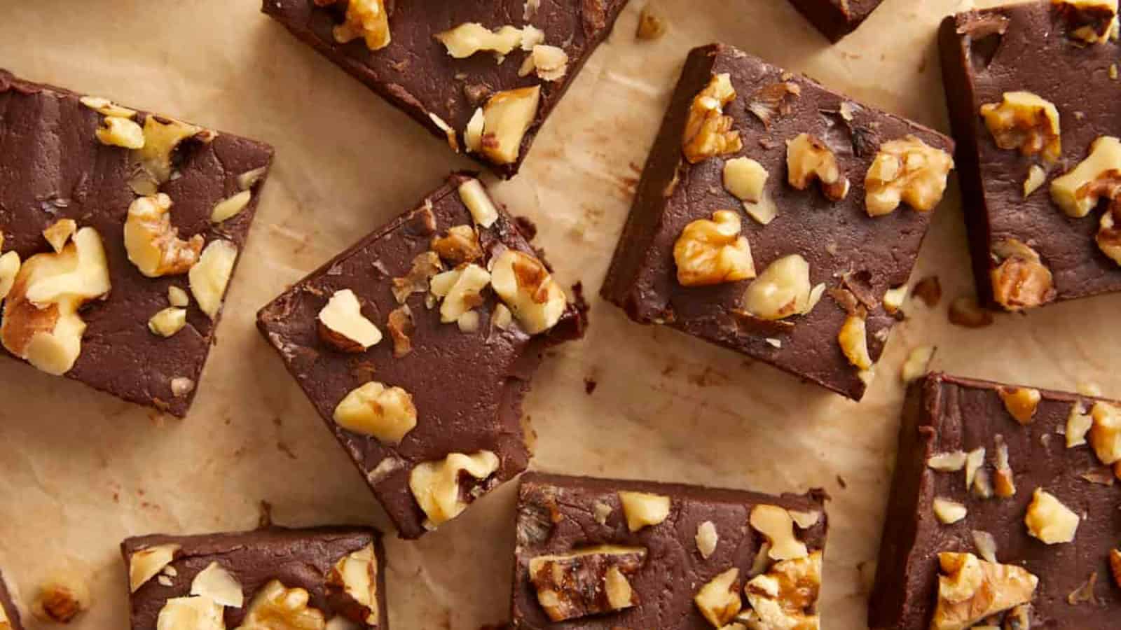 Squares of chocolate fudge topped with chopped walnuts on parchment paper.