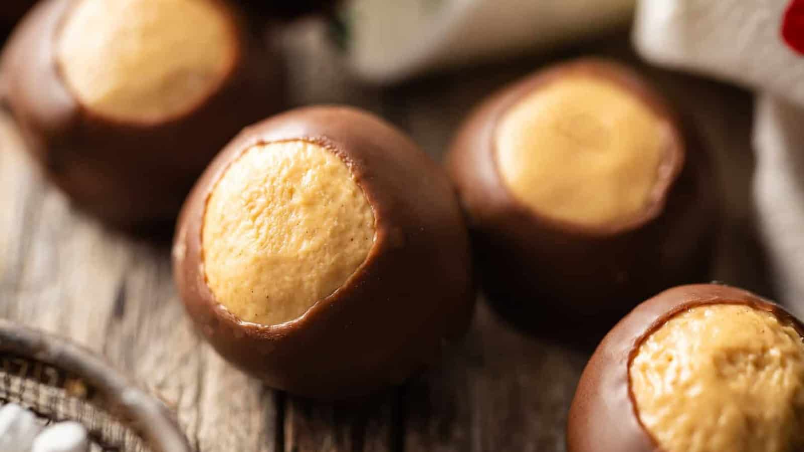 Close-up of chocolate-covered peanut butter balls, known as buckeyes, resting on a rustic wooden surface. The smooth chocolate coating partly reveals the creamy peanut butter center.