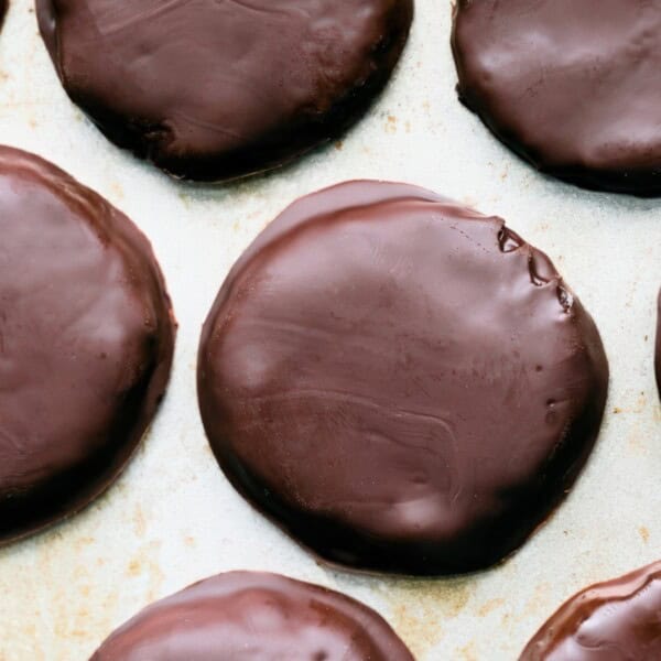 Overhead view of several round, chocolate-coated cookies arranged on a light-colored surface. The glossy chocolate covering each cookie gives them a smooth and shiny appearance.