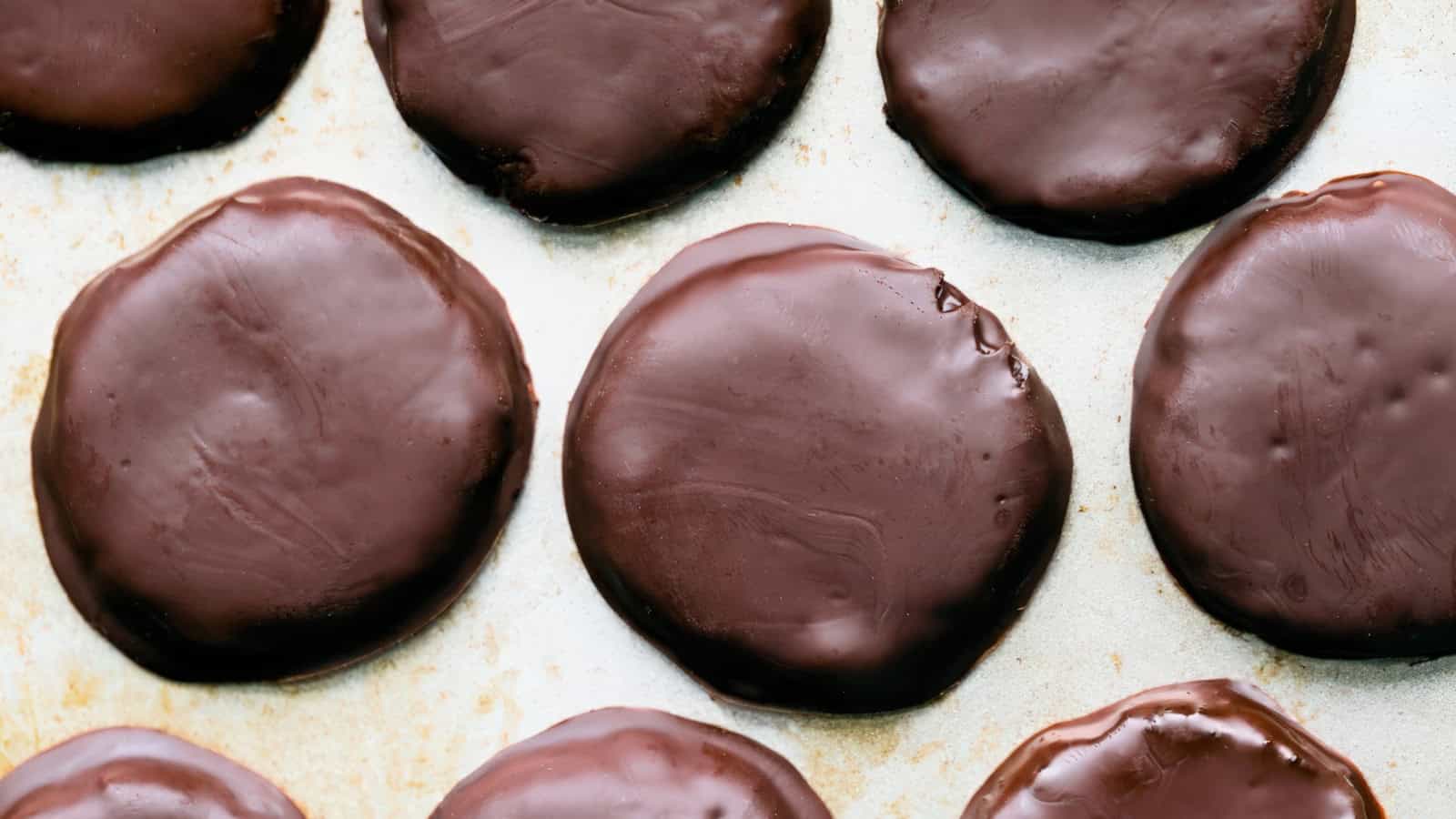 Overhead view of several round, chocolate-coated cookies arranged on a light-colored surface. The glossy chocolate covering each cookie gives them a smooth and shiny appearance.