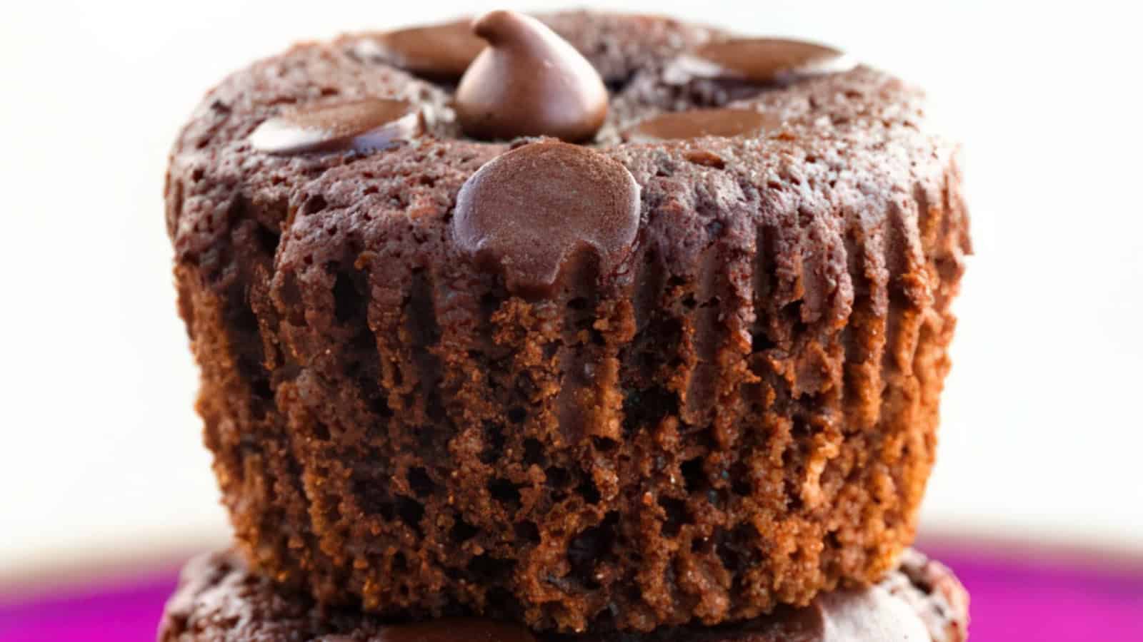 Close-up of a chocolate cupcake topped with chocolate chips. The rich, moist texture is visible, with a slightly crumbly edge and a soft, melted chocolate chip center. The background is softly blurred.