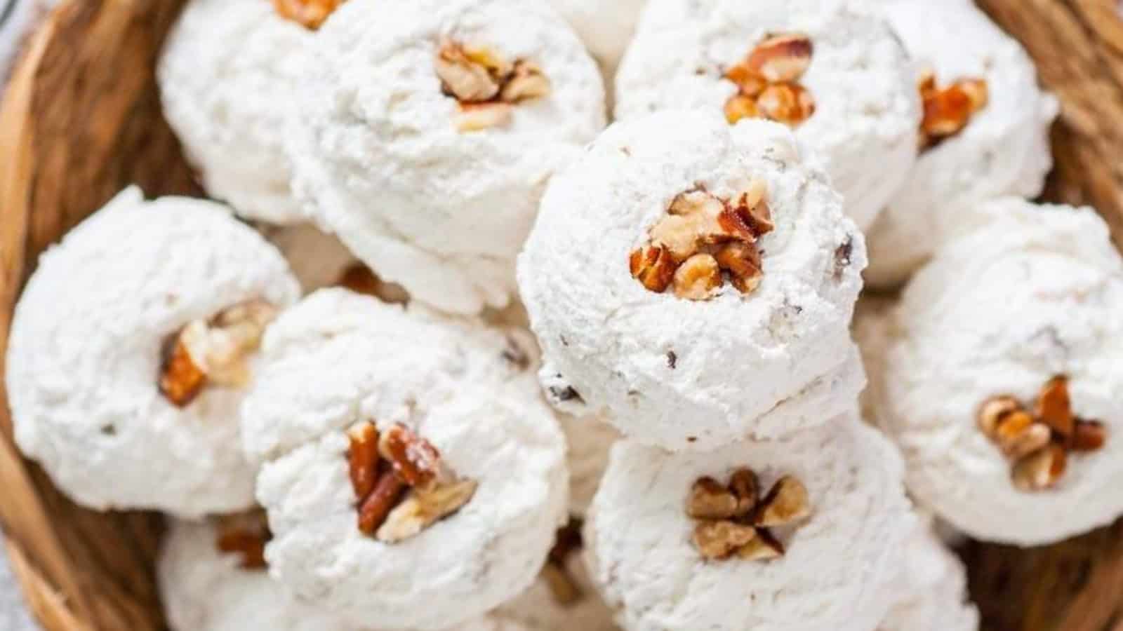 A close-up of a basket filled with round, white cookies topped with chopped nuts. The cookies appear crumbly and powdered with sugar, showcasing a rustic texture.