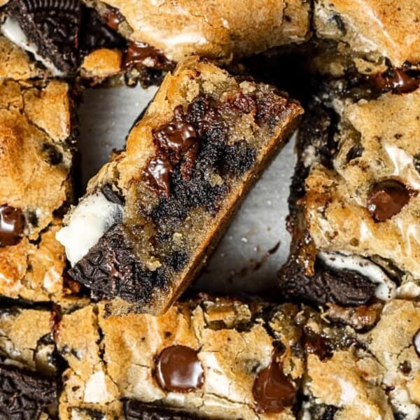 Close-up of cookie bars featuring chocolate chips and Oreo pieces, with one piece slightly elevated from the rest.