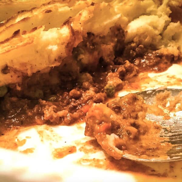 A shepherd's pie casserole in a baking dish with a serving spoon, mashed potato topping, and visible meat filling layers.