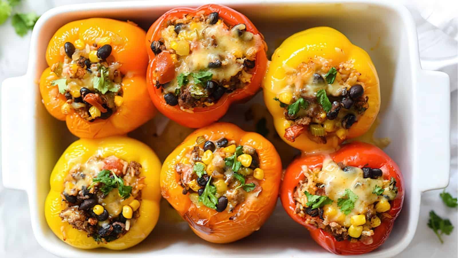 A baking dish with colorful stuffed bell peppers filled with black beans, corn, quinoa, melted cheese, and herbs. The peppers are baked and garnished, displaying vibrant reds, yellows, and oranges.