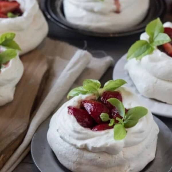 The image features plates of sweet meringue nests topped with strawberries and mint leaves, surrounded by cutlery and a jar of jam.