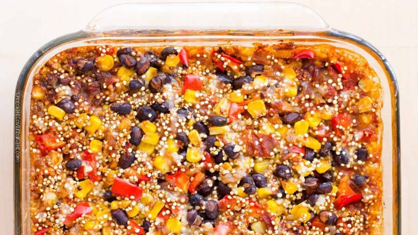 A colorful casserole in a glass dish featuring quinoa, black beans, corn, red bell peppers, and a tomato-based sauce.