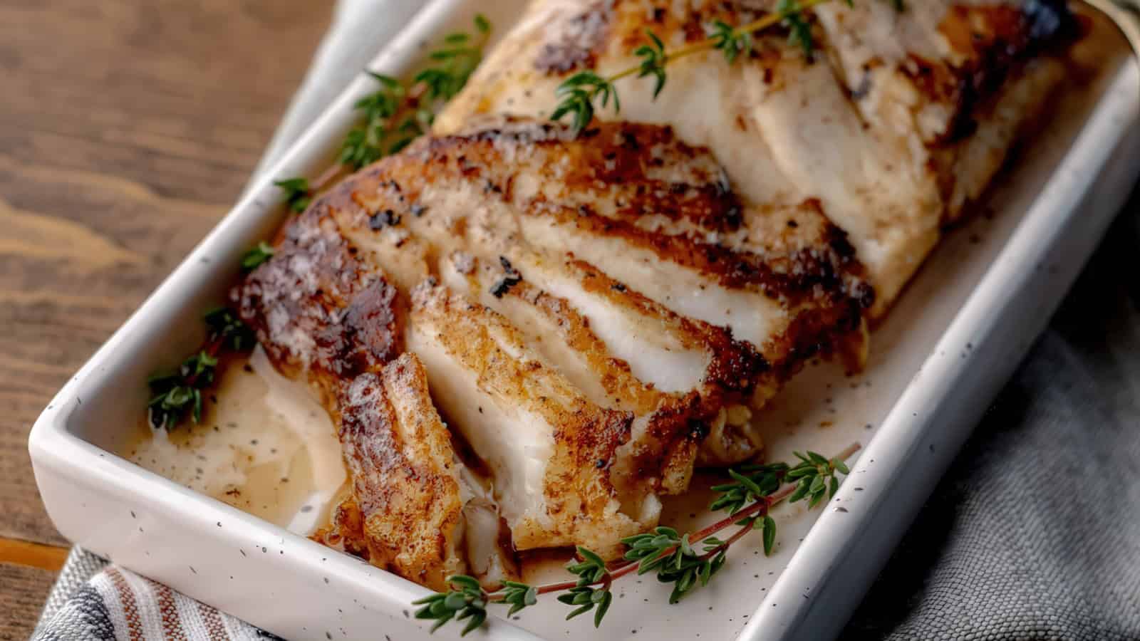 A wooden tray holds a beautifully roasted and sliced chicken breast, garnished with fresh thyme sprigs. The chicken is golden brown and juicy, set on a striped cloth, creating an inviting and rustic presentation.