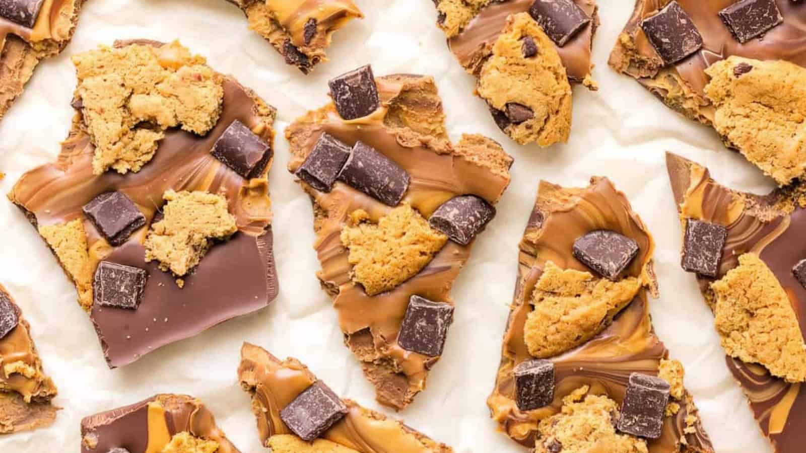 Pieces of chocolate bark topped with cookie chunks and dark chocolate squares are displayed on parchment paper. The bark has a swirled pattern of milk and dark chocolate.