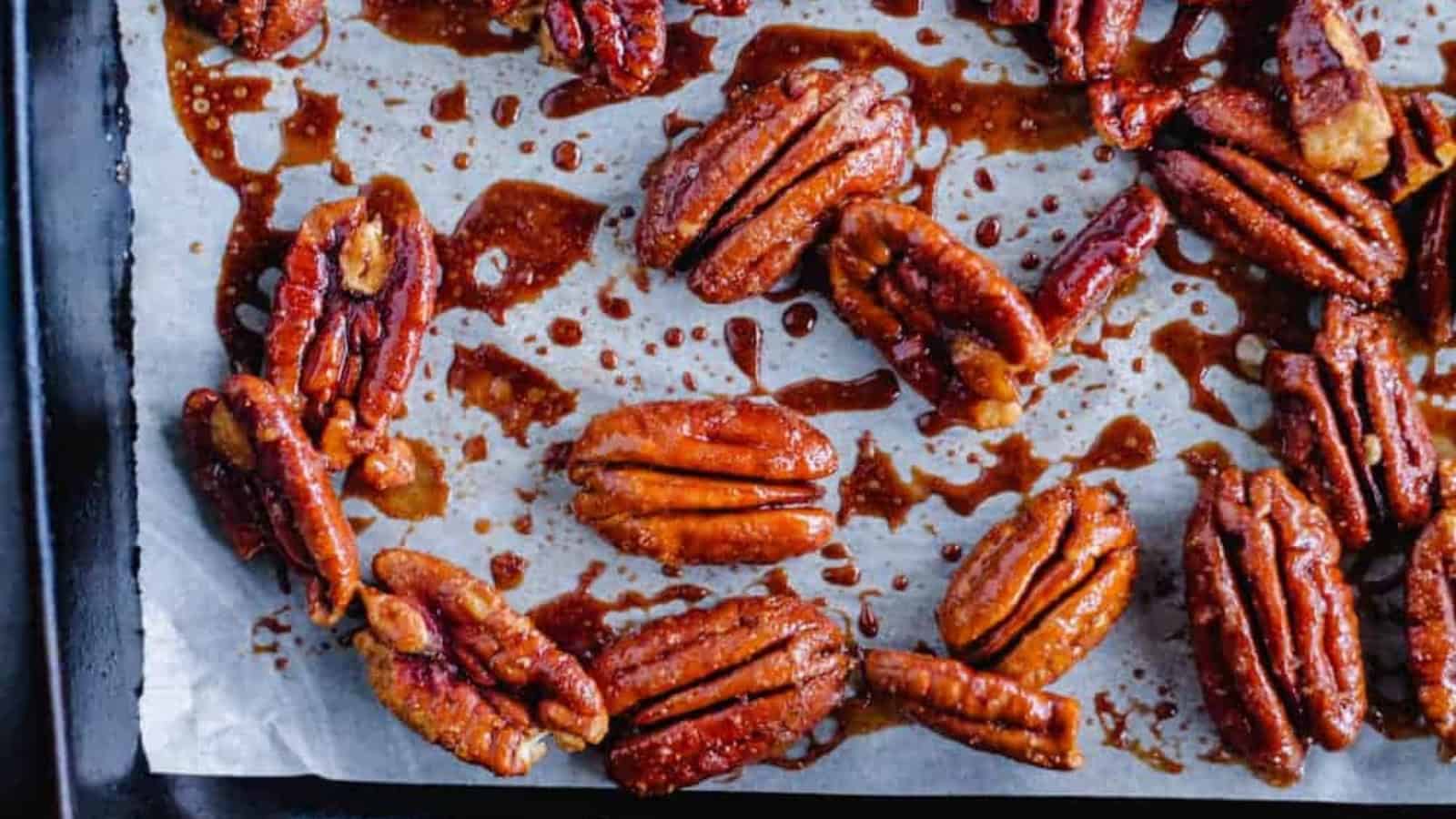 Close-up of glazed pecans on a parchment-lined baking tray. The pecans are coated in a shiny, caramelized glaze, giving them a rich and appetizing appearance.