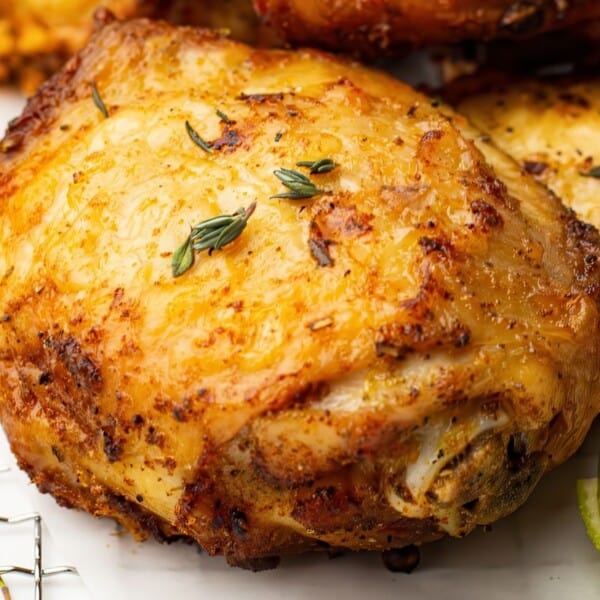 A seasoned, roasted chicken thigh garnished with herbs, accompanied by lime wedges. Served with