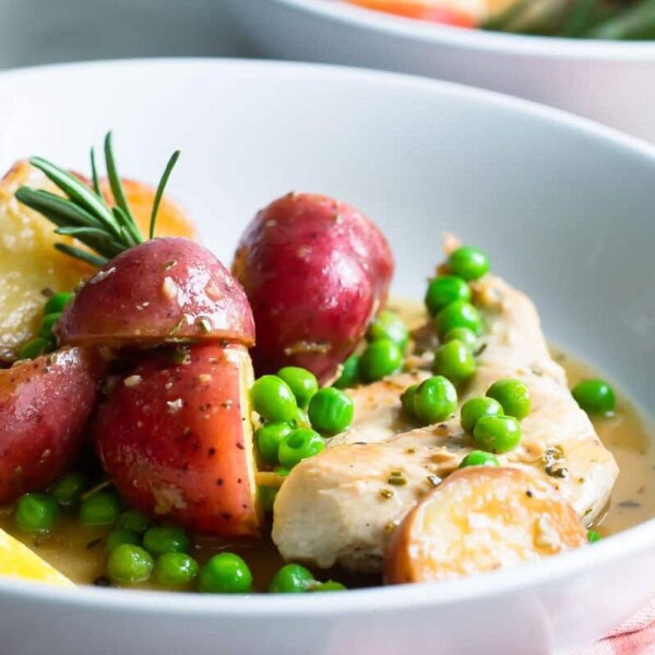 The image shows cooked red potatoes, green peas, and tender chicken breast, garnished with rosemary and accompanied by a light sauce.