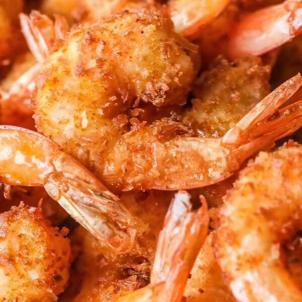Close-up of golden-brown, breaded fried shrimp with tails on, neatly arranged on a plate.