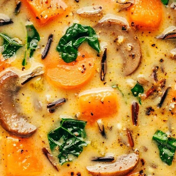 Close-up of a creamy soup with sliced mushrooms, chopped carrots, wild rice, and spinach. The soup is garnished with cracked black pepper and has a thick, hearty appearance.