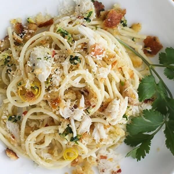 A plate of spaghetti topped with shredded crab meat, breadcrumbs, lemon slices, and parsley. Served with