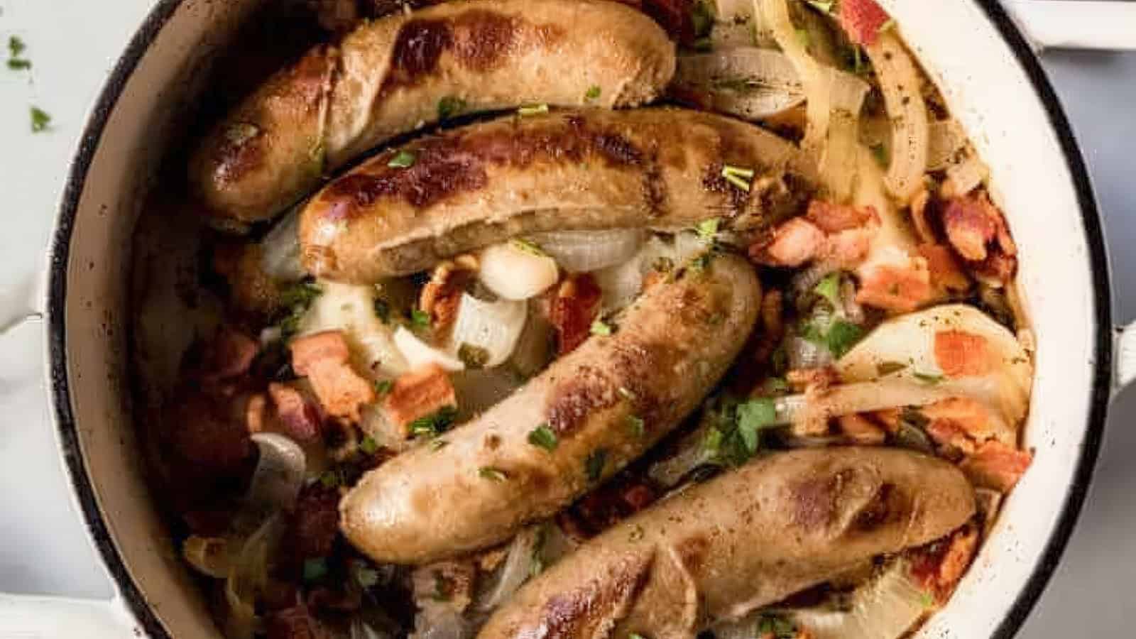 A white pot filled with browned sausages, sliced onions, bacon pieces, and chopped parsley. The dish appears savory and well-cooked, with a mix of textures and colors from the ingredients.