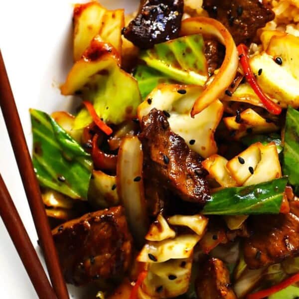 The image shows a plate of stir-fried beef with vegetables and sesame seeds, accompanied by fried rice. Chopsticks are placed on the side.