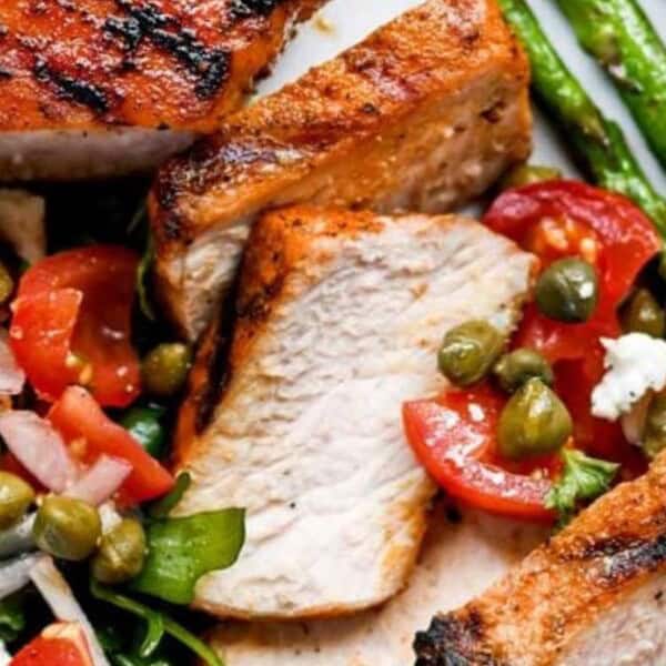 Grilled chicken slices paired with a fresh salad including arugula, cherry tomatoes, capers, red onion, and feta cheese, served alongside grilled asparagus.