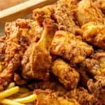 A platter of fried chicken pieces, golden fries, and a small dish of red dipping sauce.