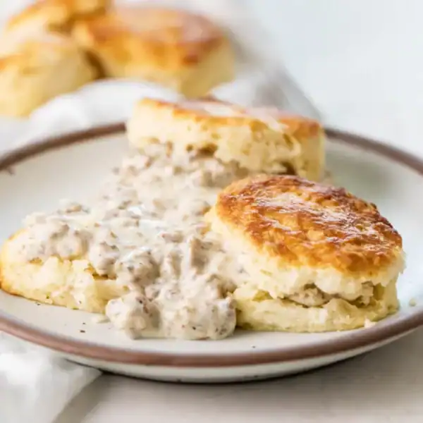 A plate of biscuits covered in creamy sausage gravy, with more plain biscuits visible in the background.