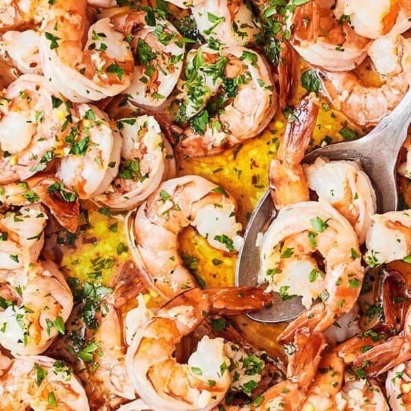 The image depicts a pan containing shrimp garnished with fresh chopped parsley and garlic, alongside a serving spoon.