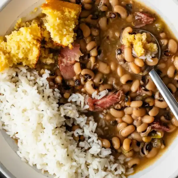 A plate with white rice, black-eyed peas with ham, a piece of cornbread, and a spoon in the bowl.