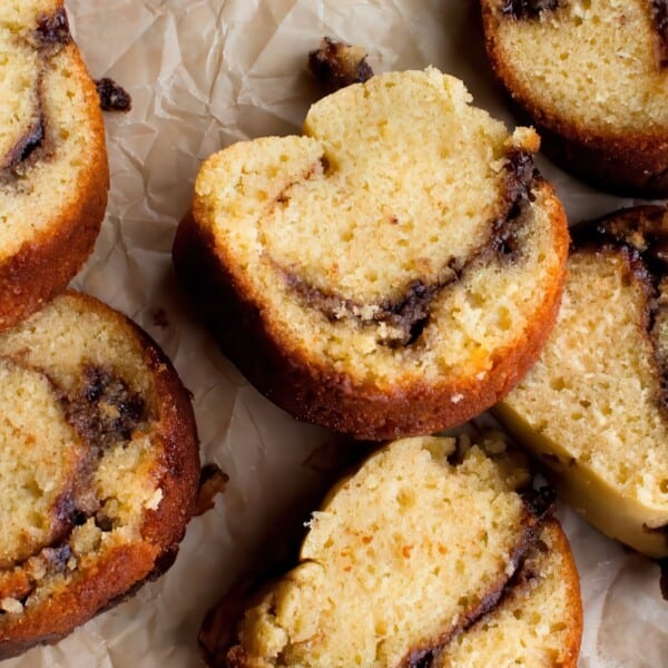 Seven slices of cinnamon swirl coffee cake are arranged on crumpled parchment paper. The cakes are golden brown with visible dark swirls of cinnamon filling, creating a marbled effect. The texture appears moist and crumbly.